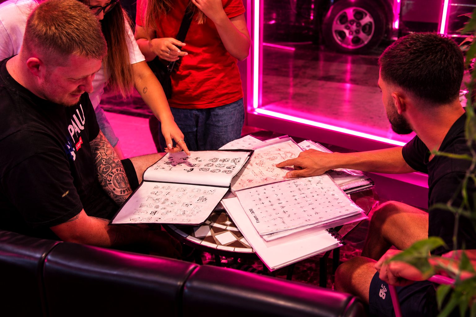 Group of friends browsing tattoo design books with the artist at Pink Shadow